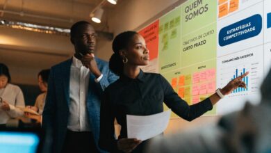 Profissional em ambiente de trabalho colaborativo analisando metas e resultados em um quadro, com colegas ao fundo, representando estratégias para lidar com a competição e crescer na carreira.