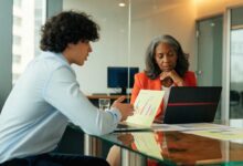 Profissional em uma reunião de negociação salarial, apresentando resultados e discutindo uma proposta com uma liderança em um escritório moderno.