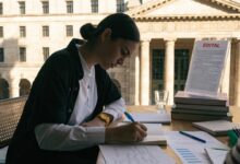 Profissional estudando um edital e fazendo anotações em uma mesa organizada, com um edifício público ao fundo, representando os primeiros passos para ingressar no serviço público brasileiro.
