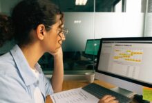 Profissional em ambiente de escritório conferindo registros de jornada e saldo do banco de horas em um computador, com calendário e anotações sobre horas de trabalho
