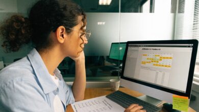 Profissional em ambiente de escritório conferindo registros de jornada e saldo do banco de horas em um computador, com calendário e anotações sobre horas de trabalho