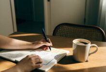Pessoa organizando uma rotina diária em um caderno, com calendário, caneta e xícara sobre uma mesa iluminada, em um ambiente tranquilo de trabalho.