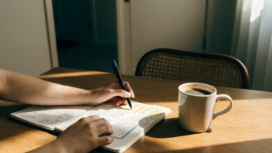 Pessoa organizando uma rotina diária em um caderno, com calendário, caneta e xícara sobre uma mesa iluminada, em um ambiente tranquilo de trabalho.